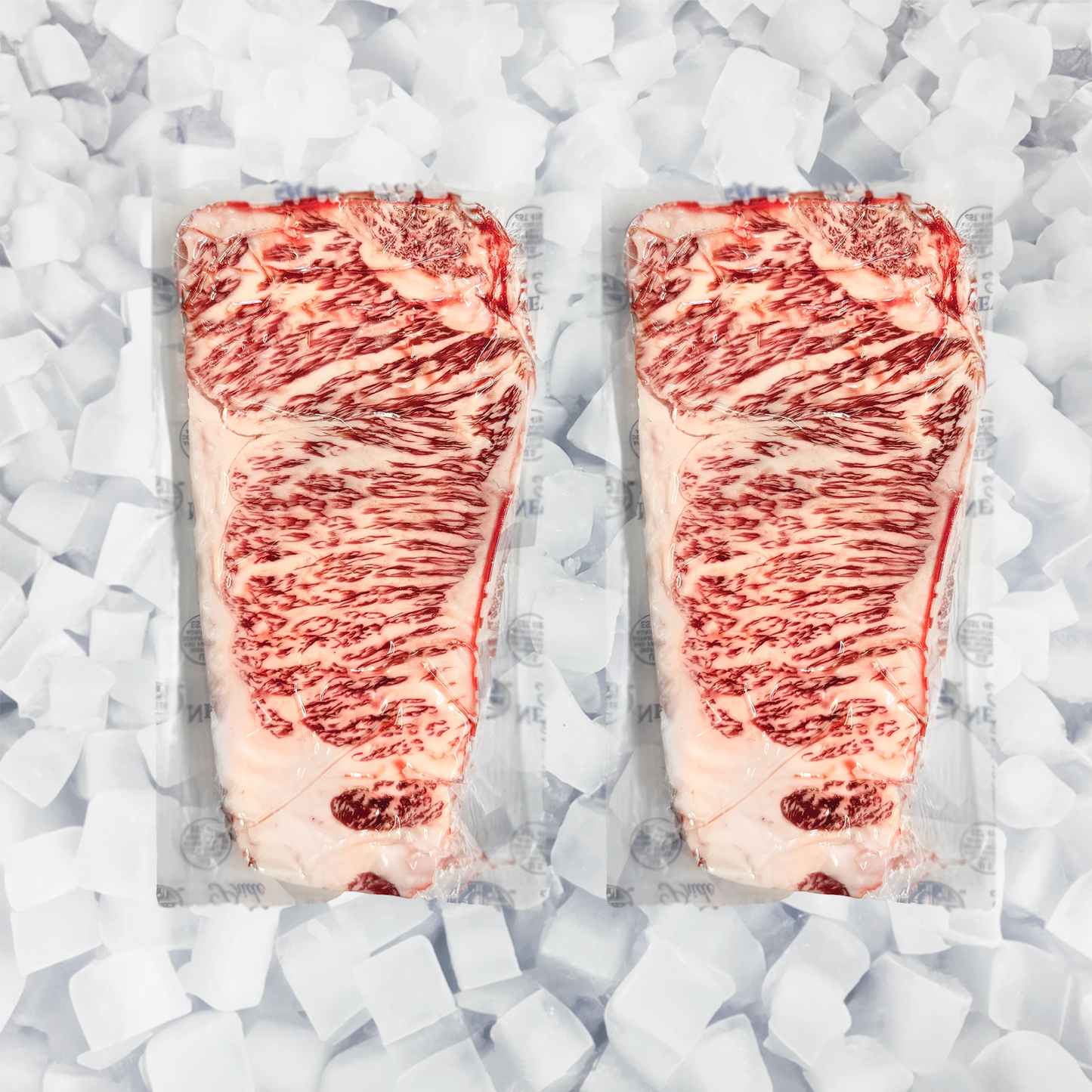 Two large marbled NY strip steaks in clear plastic packaging, arranged side by side on a bed of white ice cubes.