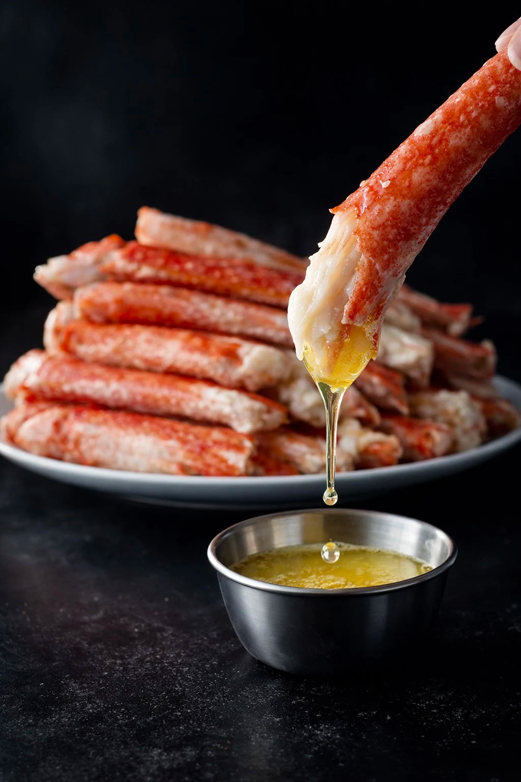 Dipping a crab leg into a bowl of butter with more crab legs in the background.