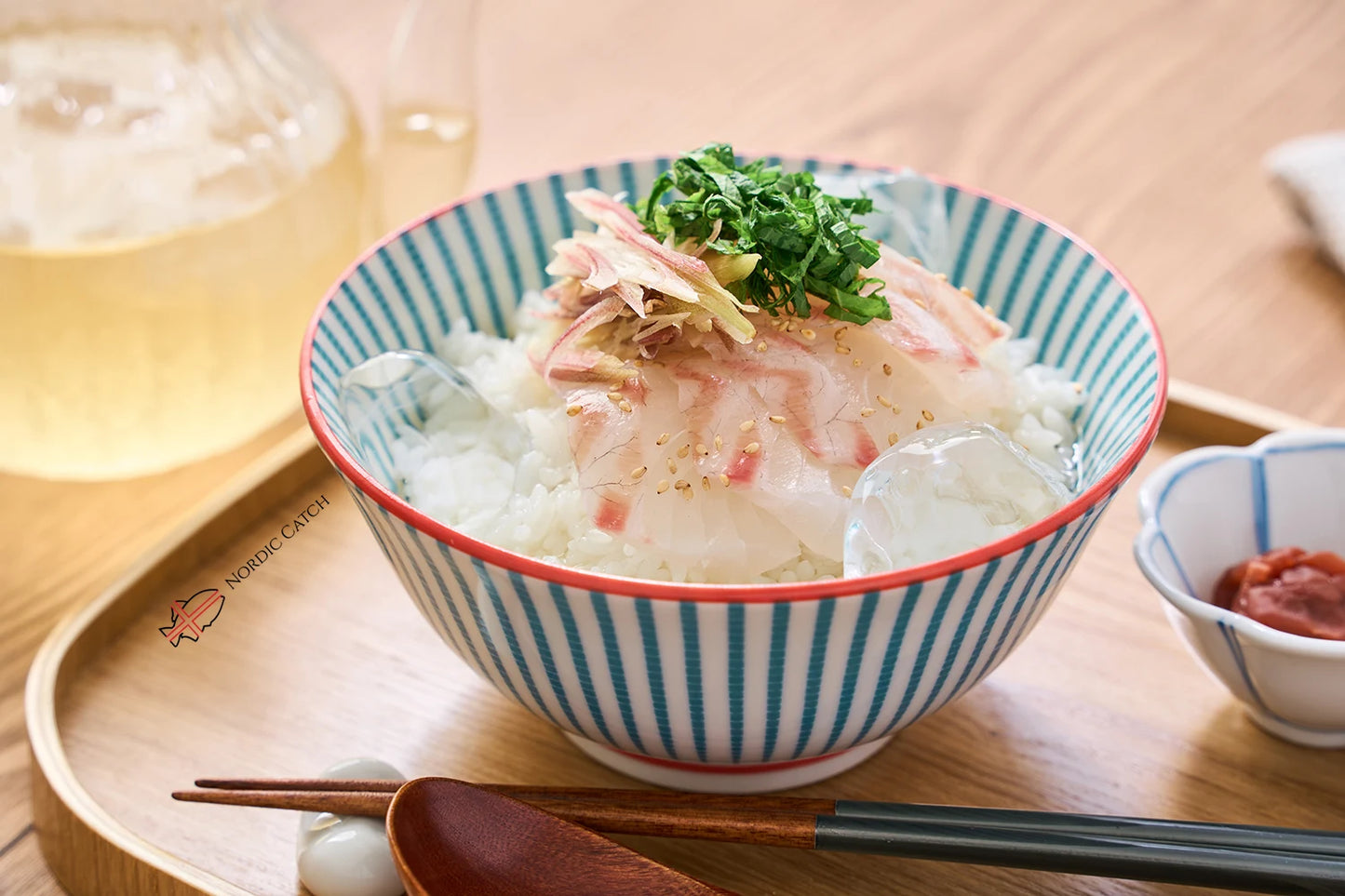 Japanese red sea bream sashimi over rice in striped porcelain bowl with scallions, ginger, daikon, and sesame seeds on Nordic Catch branded wooden tray with wooden chopsticks