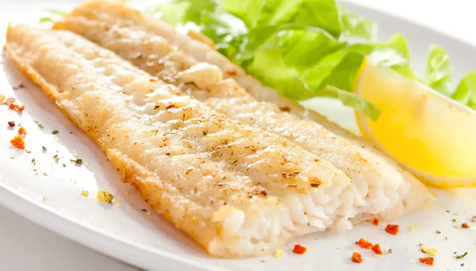 Seasoned firm white fish fillet plated with fresh greens and lemon wedge