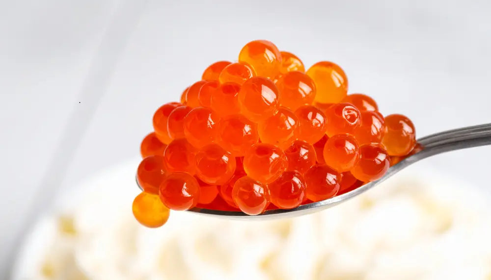 Spoon filled with vibrant red caviar pearls with glossy translucent finish
