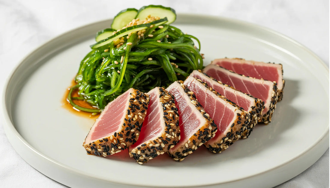 Fresh frozen seafood recipe featuring seared sesame-crusted ahi tuna slices served with seaweed salad and cucumber on a white plate