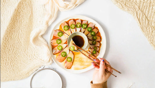 Fresh seafood nutrition showcased in a yellowtail sashimi wreath plated with jalapeño rounds in ponzu sauce, served with a soy dipping bowl and chopsticks