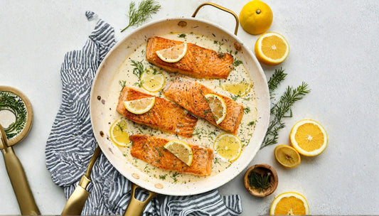 lemon dill salmon recipe with four pan-seared fillets in creamy sauce with lemon slices and fresh dill in a speckled skillet