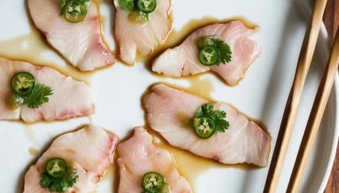 Ocean-to-table seafood served as yellowtail sashimi slices topped with jalapeño and cilantro in yuzu ponzu sauce on a white plate with chopsticks