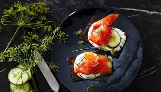 Omega-3-rich seafood open-faced on dark rye crackers with cream cheese, cucumber, fresh dill, and chives on a dark plate
