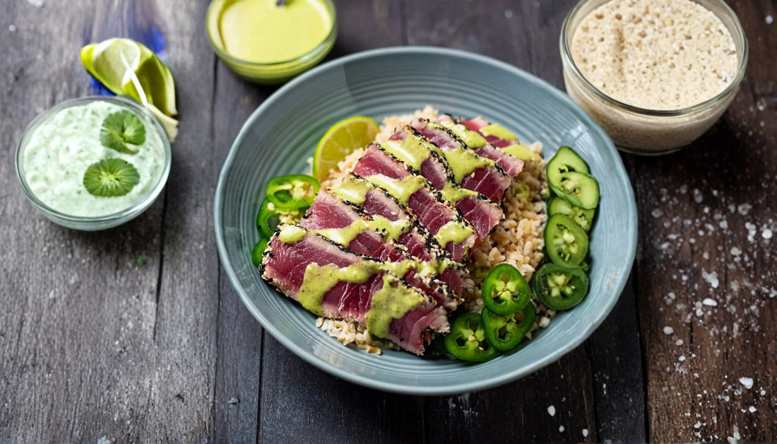 seared ahi tuna sliced over brown rice with avocado green goddess drizzle, jalapeño, and cucumber slices in a blue bowl