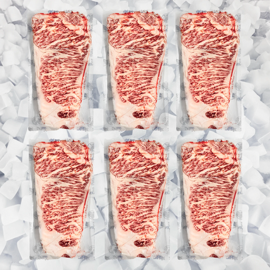 Six raw marbled wagyu NY strip steaks in clear plastic packaging arranged in two rows on a bed of ice cubes.