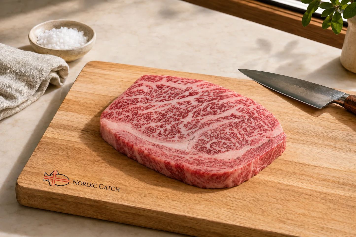A raw marbled wagyu ribeye steak rests on a wooden cutting board with the Nordic Catch logo, alongside a chef's knife, a small bowl of coarse salt, and a neutral cloth on a tabletop.