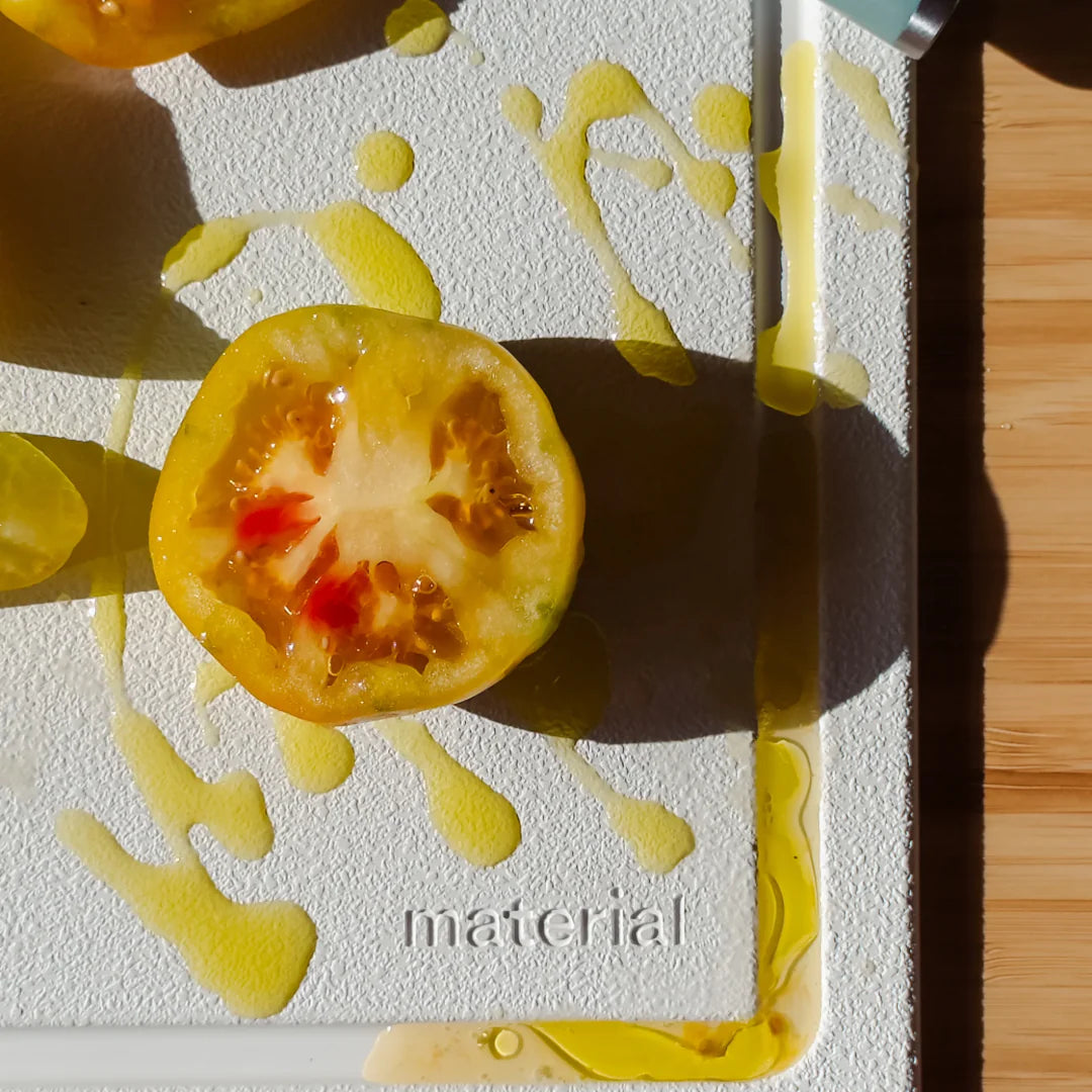 Sliced yellow heirloom tomato on white cutting board with chef knife showing juice and seeds