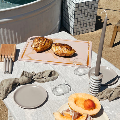Non-porous cutting board with roasted portobello mushrooms, table setting with white plates, glassware, linen napkins, and fresh fruit by the pool