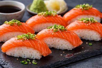 Icelandic Arctic char nigiri sushi topped with sliced scallions and sesame seeds on Nordic Catch branded black slate with soy sauce and condiments