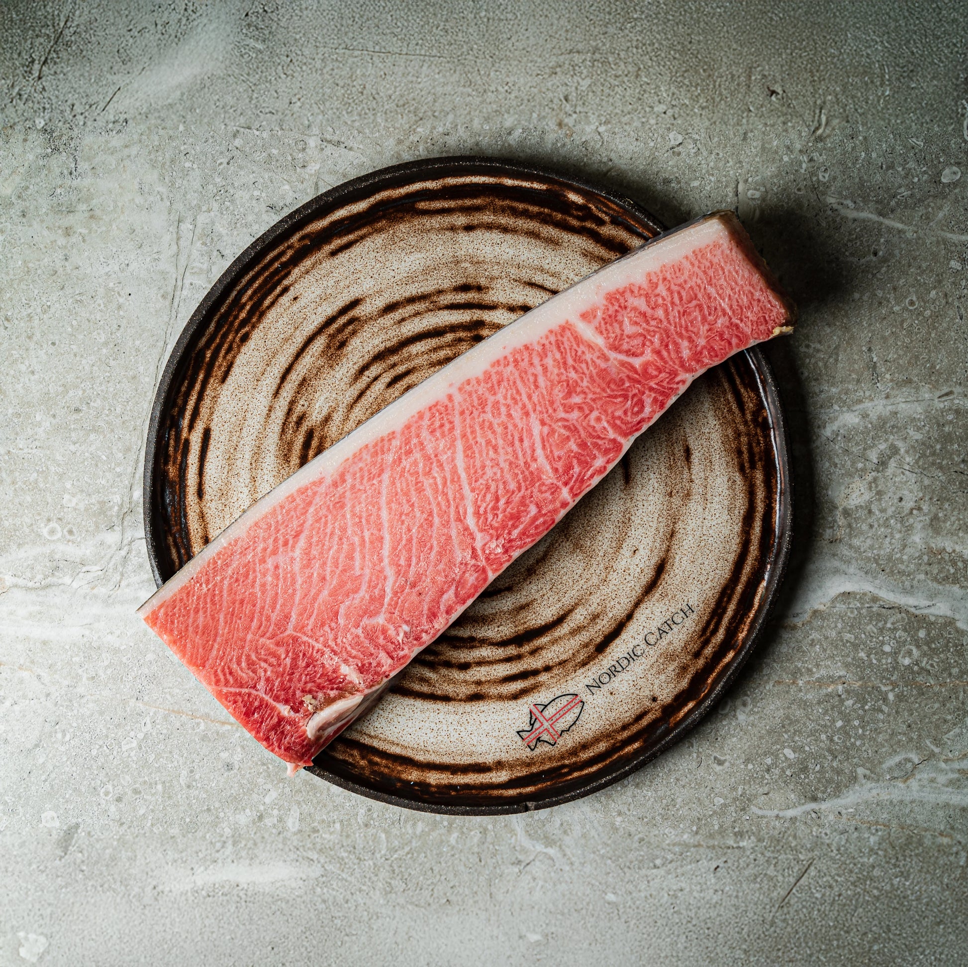 Raw marbled Bluefin on a ceramic plate with a brand logo on a concrete surface