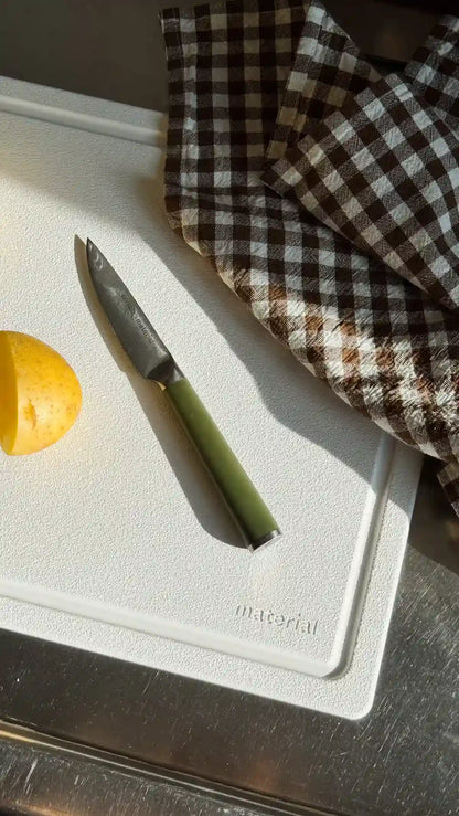 Non-toxic cutting board with chef knife and halved lemon on white surface with brown checkered kitchen towel