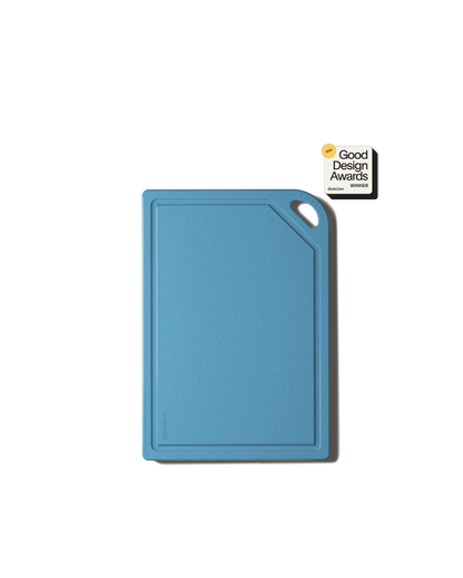Blue cutting board with juice groove and black handle displaying Good Design Awards winner certification badge on black background