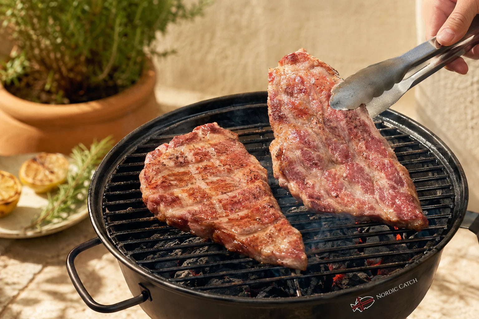 Two grilled Iberico Pluma steaks cooking on a round black charcoal grill with tongs holding one steak, set outdoors on a stone surface with a potted plant in the background.