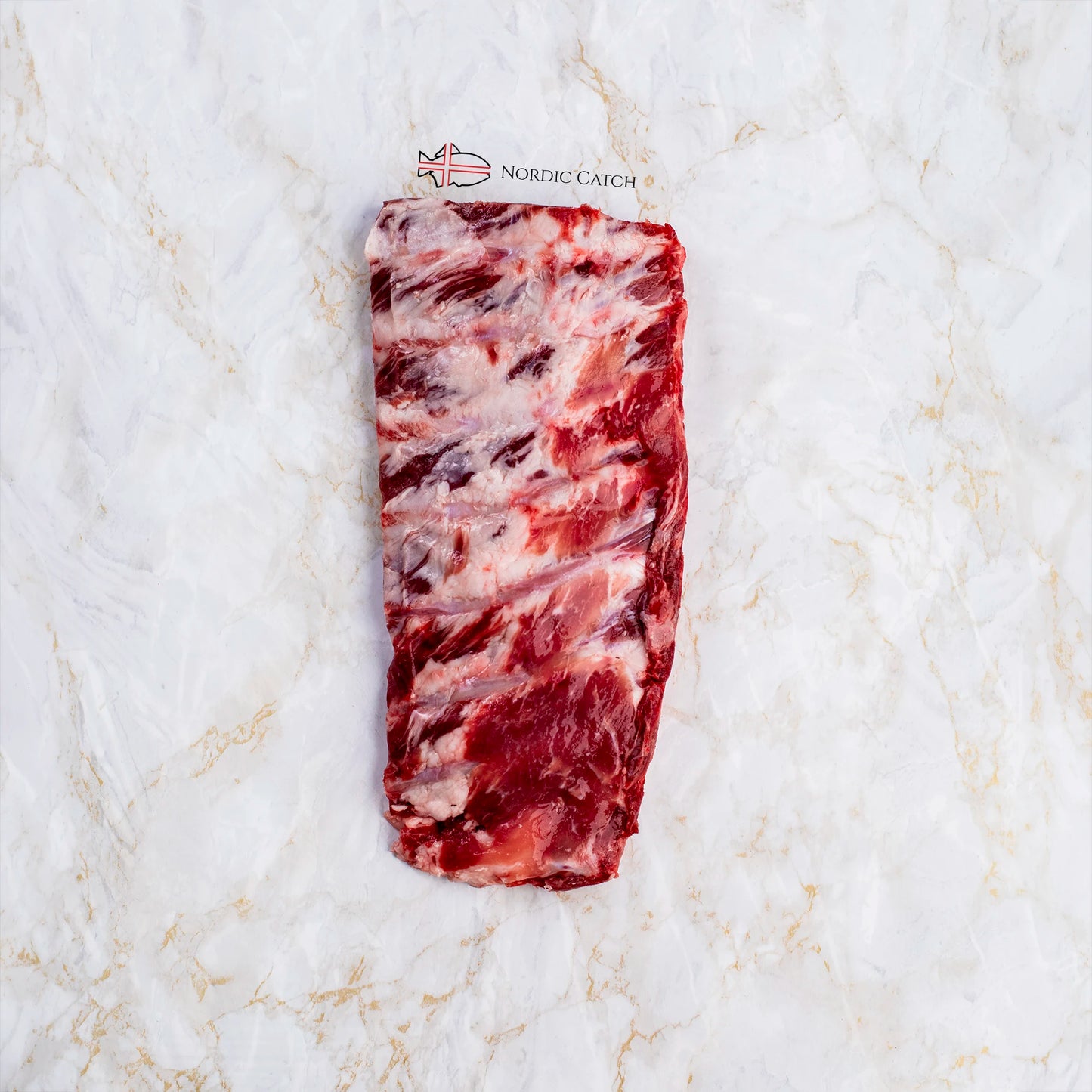 A raw cut of marbled Iberico ribs costilla photographed from above on a white marble surface. A small 'NORDIC CATCH' logo is printed above the product.