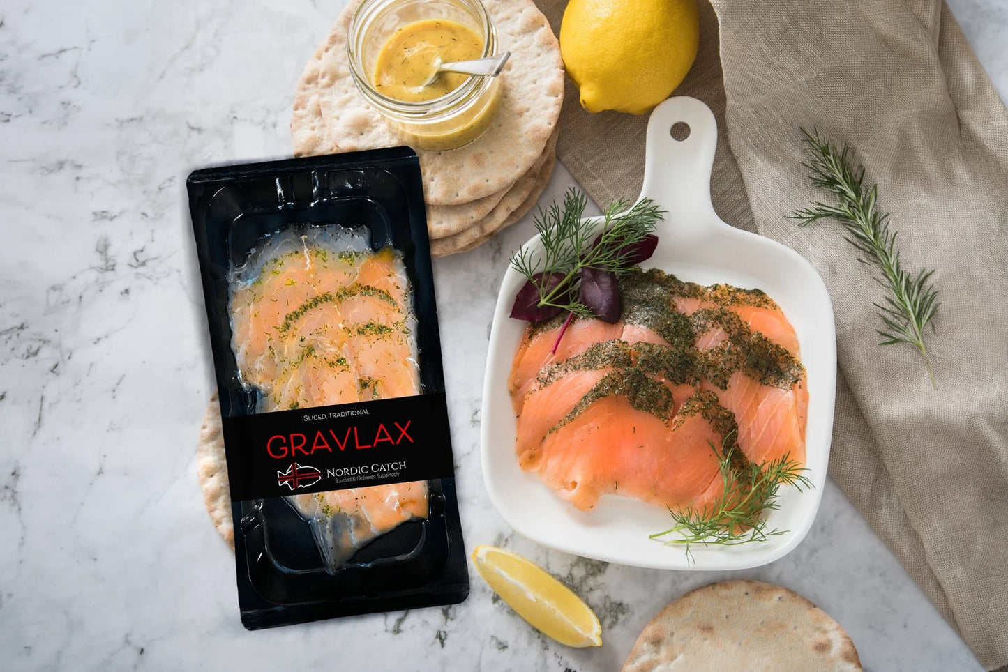 Cured salmon served on white plate with fresh dill, lemon, capers, whole grain mustard, and crackers on marble surface