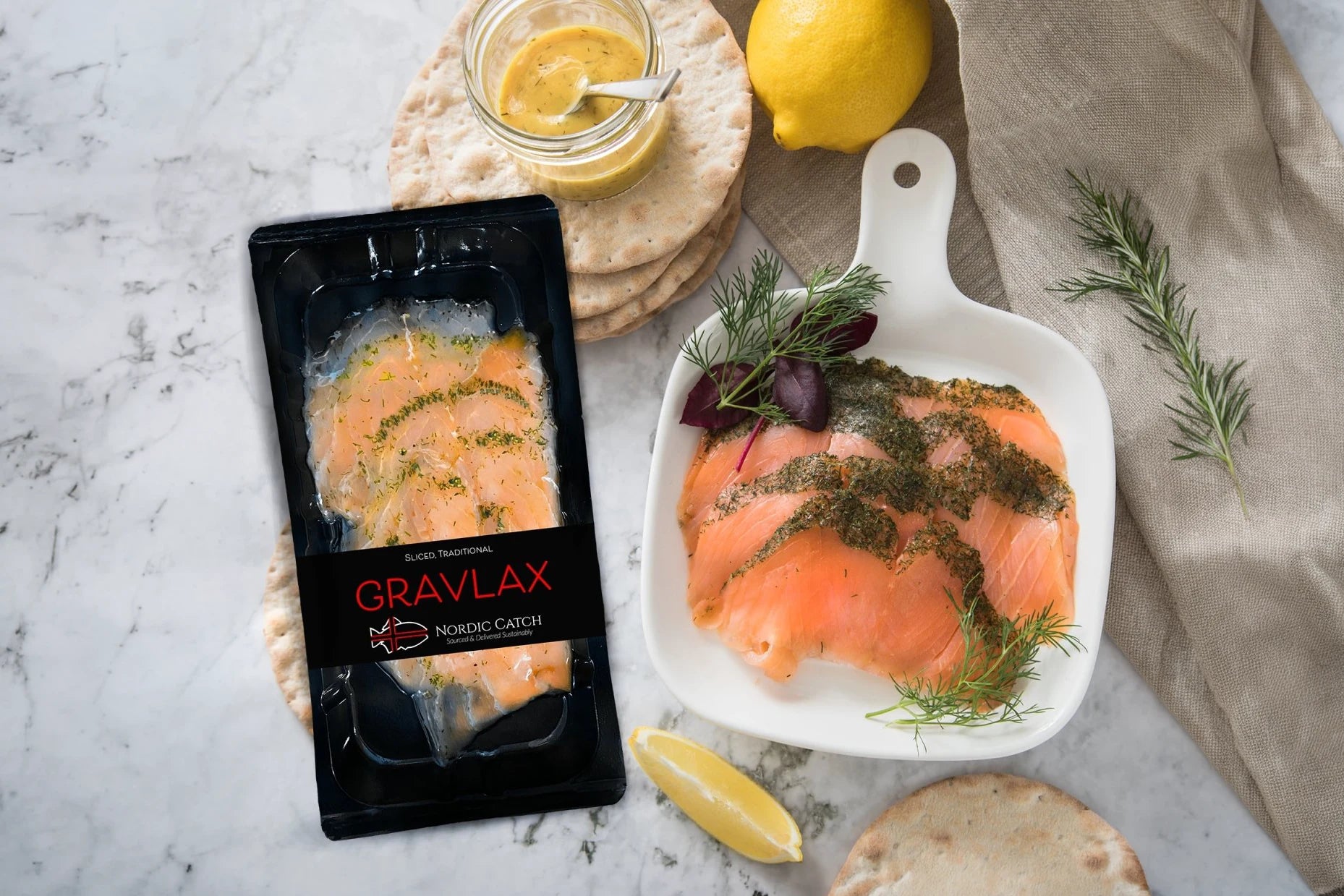 Cured salmon served on white plate with fresh dill, lemon, capers, whole grain mustard, and crackers on marble surface