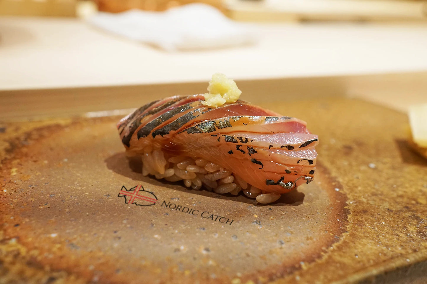 Mackerel nigiri sushi topped with grated ginger and black sesame seeds on Nordic Catch branded wooden board