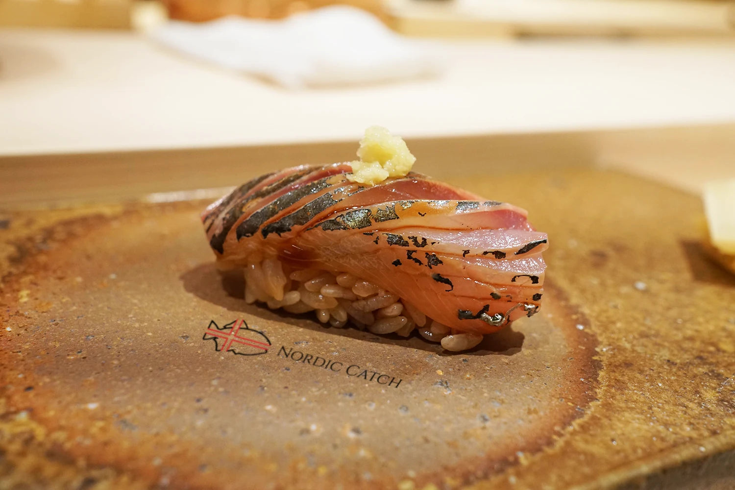 Mackerel nigiri sushi topped with grated ginger and black sesame seeds on Nordic Catch branded wooden board