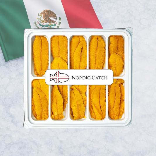A top-down view of a white plastic tray filled with bright orange-yellow fresh sea urchin roe, with a white label reading 'NORDIC CATCH' across the center. A Mexican flag is partially visible in the background on a light marbled surface.