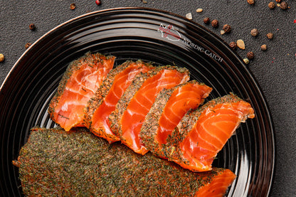 Sliced smoked salmon on a black plate with spices on a dark surface