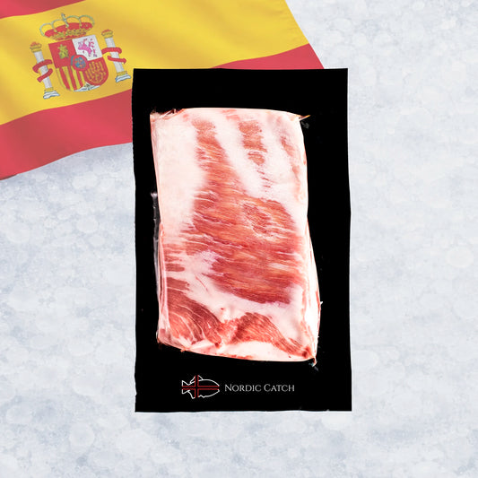 A vacuum-sealed pack of raw Iberico pork belly meat with fat layers, placed on a black card over a Spanish flag and a light icy background. The card shows the brand name Nordic Catch.