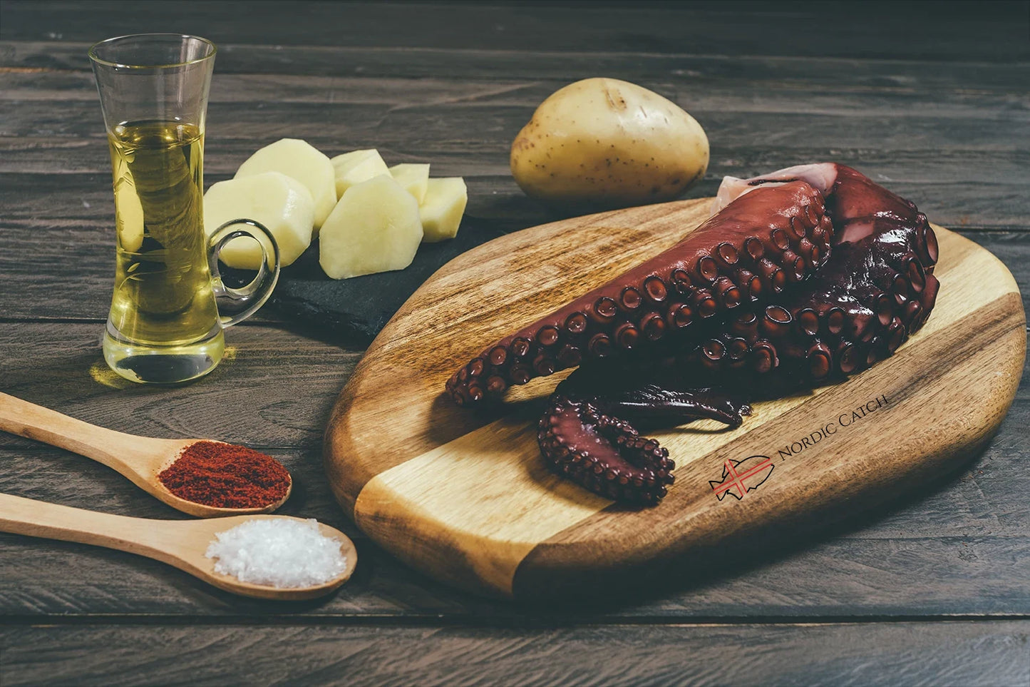 Wooden cutting board with octopus, potatoes, and a glass of oil on a wooden surface.