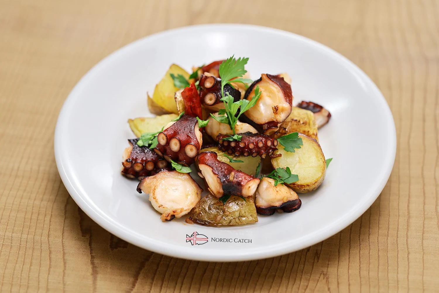 Plated dish of octopus and potatoes with herbs on a wooden surface, featuring the Nordic Catch logo.