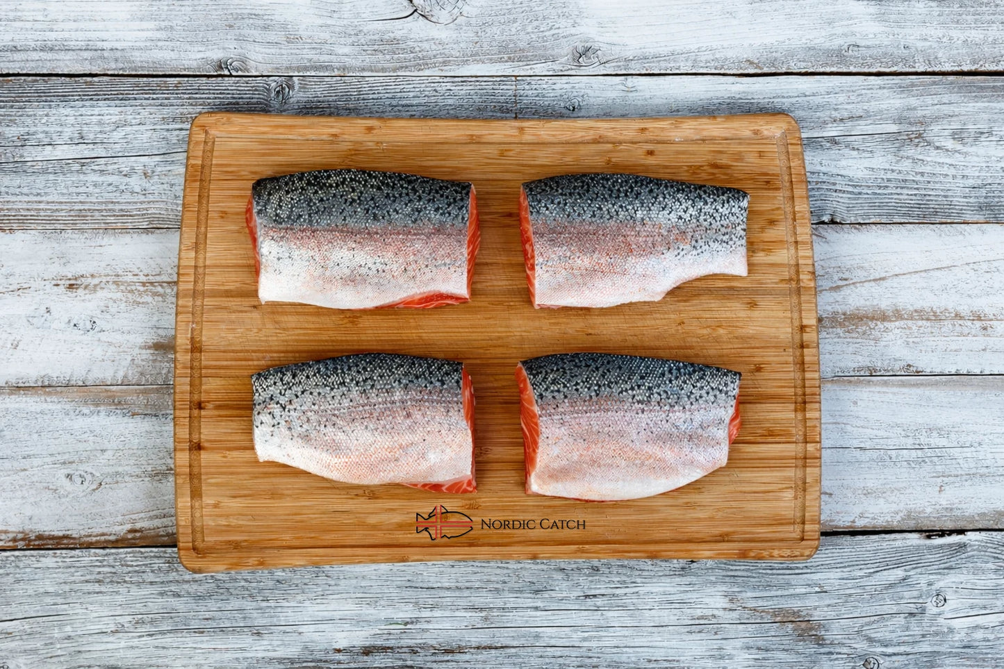 Icelandic steelhead trout skin-on fillets displayed on Nordic Catch branded bamboo cutting board on whitewashed wooden surface
