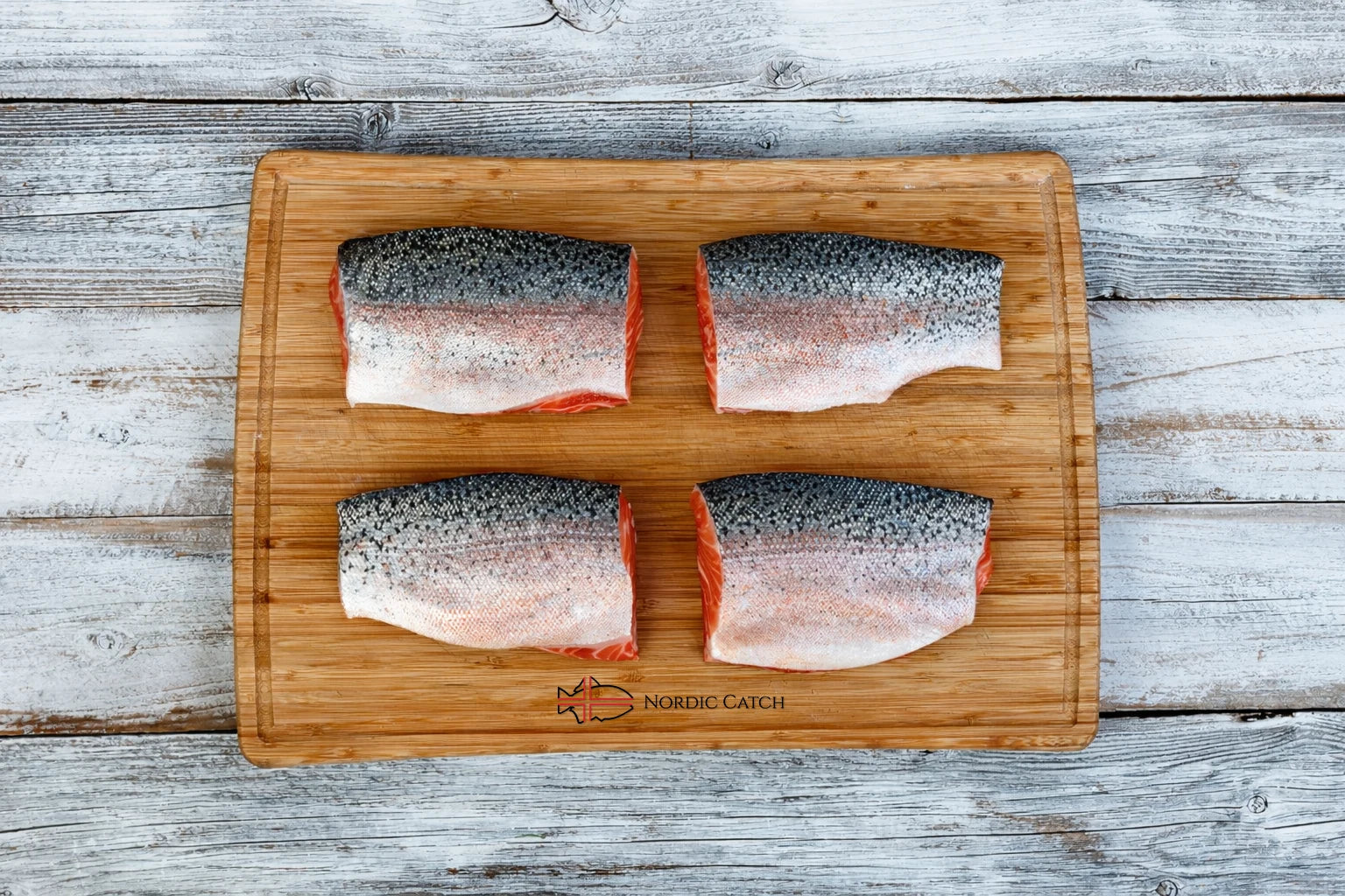 Icelandic steelhead trout skin-on fillets displayed on Nordic Catch branded bamboo cutting board on whitewashed wooden surface