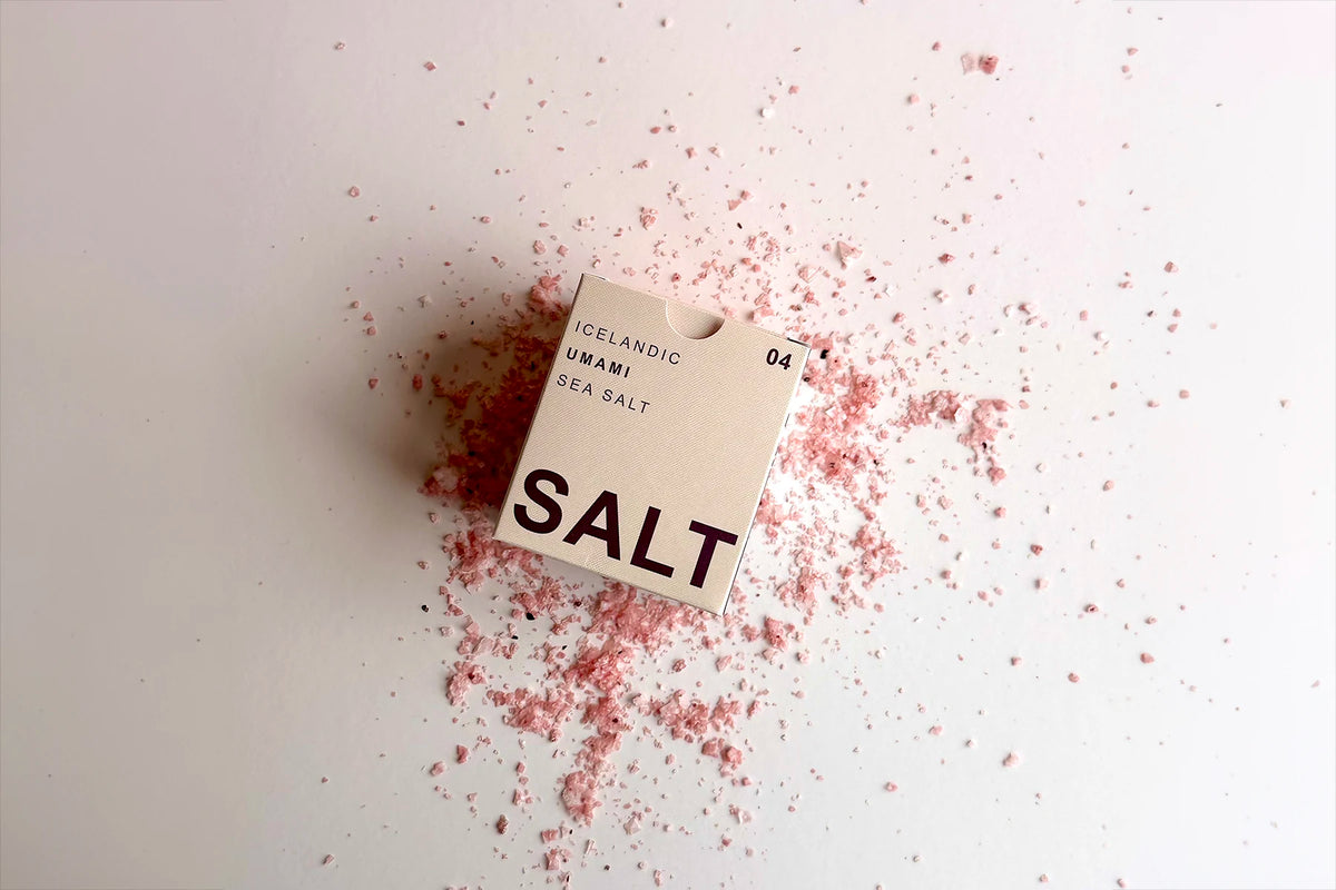 A pink box of sea salt sitting on top of a bed of flaky sea salt in with a pink color