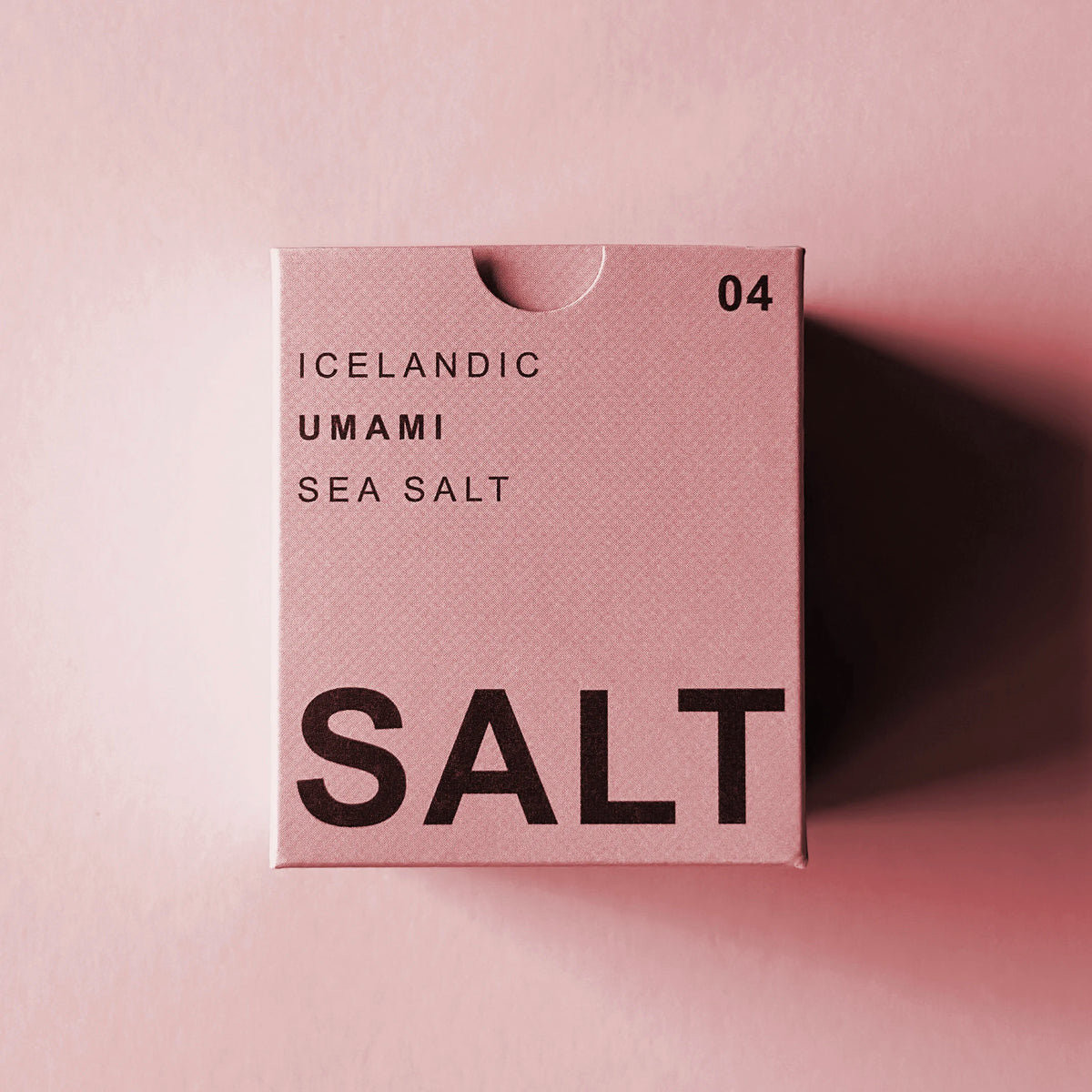 A square pink box of Icelandic Umami Sea Salt with bold black text, photographed on a matching pink background with a soft shadow cast to the right.