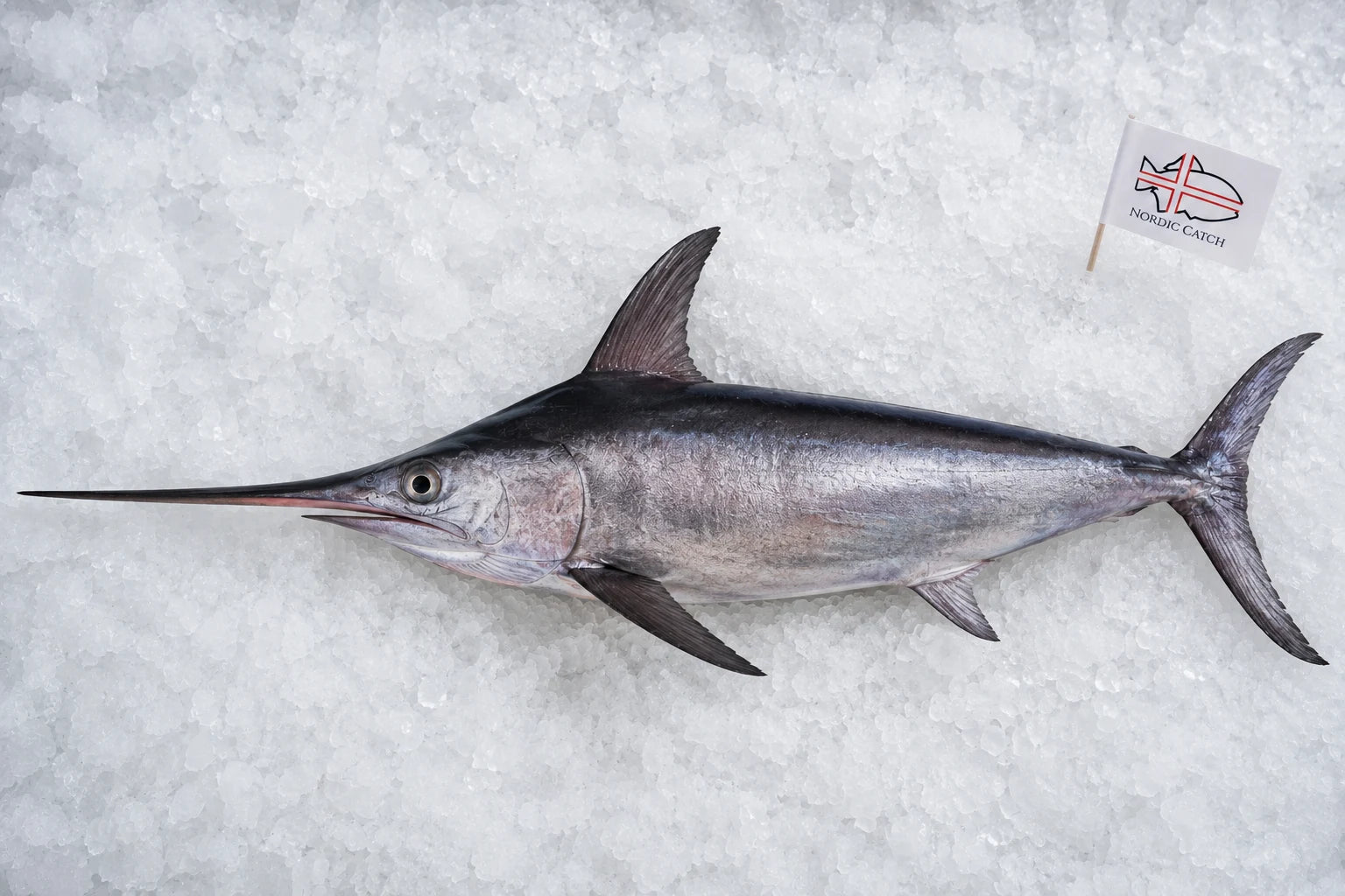 A whole blue swordfish laid flat on crushed ice, with a small 'Nordic Catch' flag near the top right.