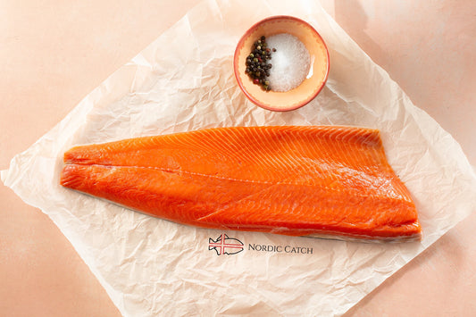 Raw salmon fillet on a piece of paper with a small bowl of salt and pepper, branded 'Nordic Catch'.
